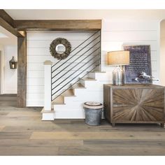 a room with white walls and wood floors, a stair case and a wooden table