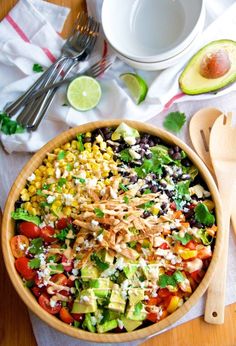 a salad in a wooden bowl with avocado and cilantro on the side