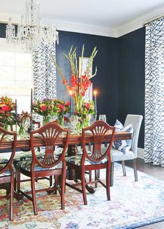 a dining room table with chairs and flowers in vases on the top, next to a chandelier