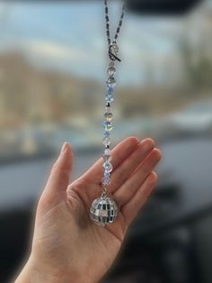 a hand holding a silver and crystal beaded necklace in front of a car window