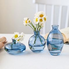 three vases with flowers in them sitting on a table next to an open book