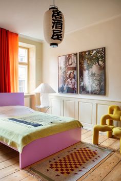 a bed sitting in a bedroom next to a window with red drapes on the windowsill