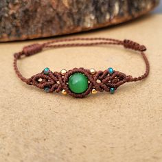 a green beaded bracelet sitting on top of a wooden table next to a rock