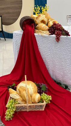 a table topped with a basket filled with bread and grapes next to a white table cloth