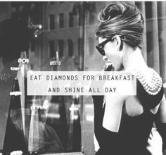 a woman is talking on her cell phone while walking down the street with a sign that says eat diamonds for breakfast and shine all day