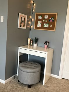 a white desk with a grey ottoman underneath it and lights on the wall behind it