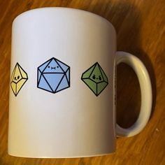 a white coffee mug with three different colored origami shapes painted on it's side