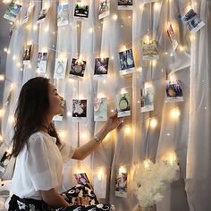 a woman is hanging pictures on the wall with fairy lights and string lights behind her