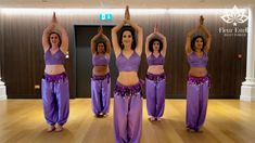 a group of women standing on top of a wooden floor in purple pants and bras