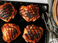 four steaks cooking on a grill with tongs and a plate next to them