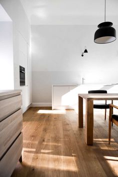 an empty kitchen with wooden floors and white walls, along with black pendant lights hanging from the ceiling