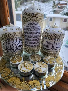 the candles are decorated with arabic calligraphys and gold leaf decorations on a tray in front of a window