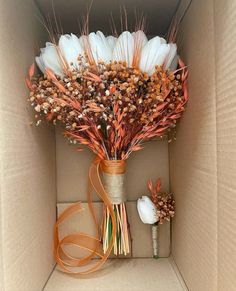 an arrangement of dried flowers in a cardboard box with ribbon on the bottom and inside