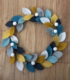 a wreath made out of felt leaves and pom poms on a wooden floor