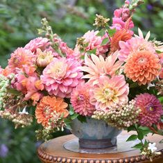 a vase filled with pink and orange flowers on top of a wooden table in front of trees