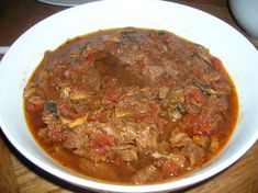 a white bowl filled with stew on top of a wooden table