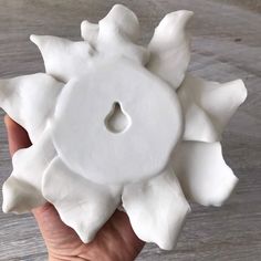 a hand holding a white ceramic object in the shape of a sunflower on a wooden table