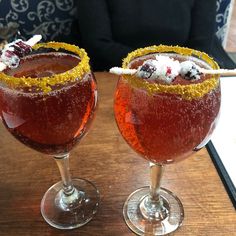 two glasses filled with drinks sitting on top of a wooden table next to each other