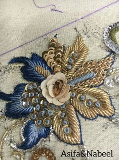 an embroidered piece with gold, blue and white flowers on it's side is shown