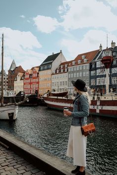 a woman standing on a dock next to boats in the water and buildings behind her