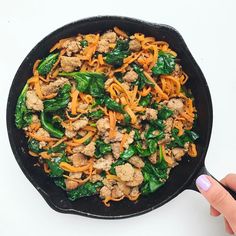 a skillet filled with meat, noodles and spinach on top of a white table