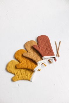 four oven mitts are lined up next to matches on a white surface with an orange, yellow, and red design