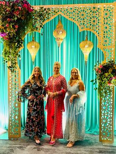 three women standing next to each other in front of a blue backdrop with flowers on it