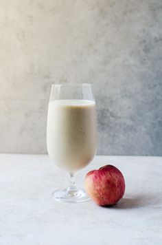 an apple next to a glass of milk on a white countertop with a marble background