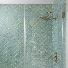 a bathroom with a glass shower door and blue mermaid scales on the wall behind it