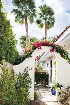 a white house with pink flowers and greenery on the front door, surrounded by palm trees