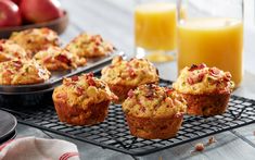 several muffins on a cooling rack with orange juice and apples in the background