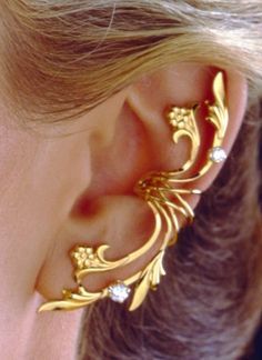 a close up of a person wearing gold ear cuffs with flowers and leaves on them