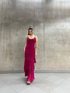 a woman standing in front of a wall wearing a purple dress and smiling at the camera