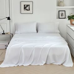 a bed with white sheets and pillows in a room next to a wall mounted shelf