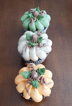 three cupcakes decorated with green and white icing on top of a wooden table