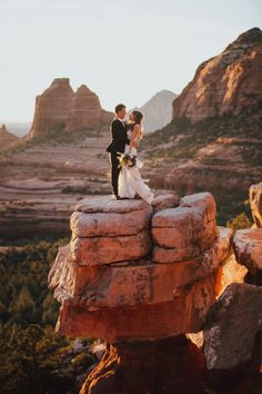 a bride and groom standing on top of a rock formation in the desert at sunset