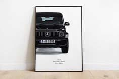 a black mercedes benz poster hanging on the wall next to a white wall and wooden floor