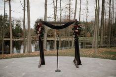 an outdoor ceremony setup with black drapes and flowers on the arch, surrounded by trees