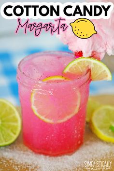 a pink lemonade cocktail with cotton candy on the top and limes around it