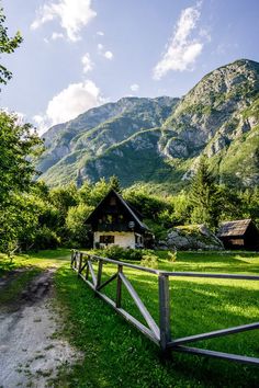 a wooden fence is in front of a small house and mountain range with green grass