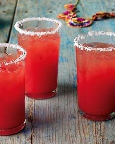 three red drinks sitting on top of a wooden table