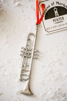 a silver trumpet ornament with a red ribbon around it on a white surface