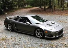 a silver sports car parked in the middle of a gravel road next to some trees