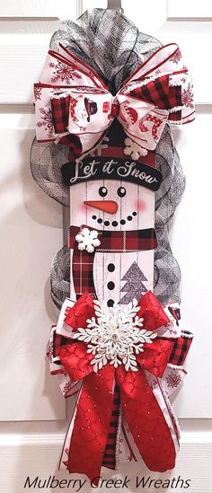 a snowman door hanger with red and white ribbons on it's side