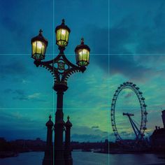 a lamp post with a ferris wheel in the background at dusk, and an overcast sky