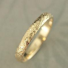 a gold wedding ring with an intricate design on the outside and inside, sitting on a plain surface