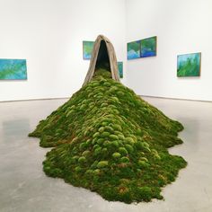 a pile of green moss sitting in the middle of a white room with paintings on the wall