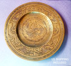 a gold plate with an intricate design on the front and sides, sitting on a purple background