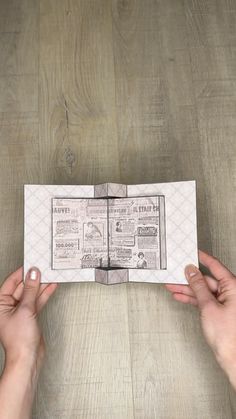 two hands holding an open newspaper on top of a wooden table