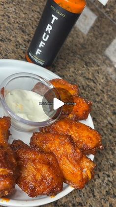 some fried food on a white plate next to a bottle of sauce and an orange drink